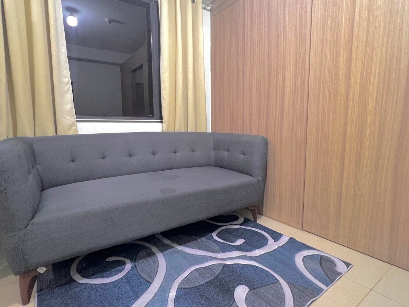 A grey sofa in a room with a wooden wardrobe and a patterned rug.