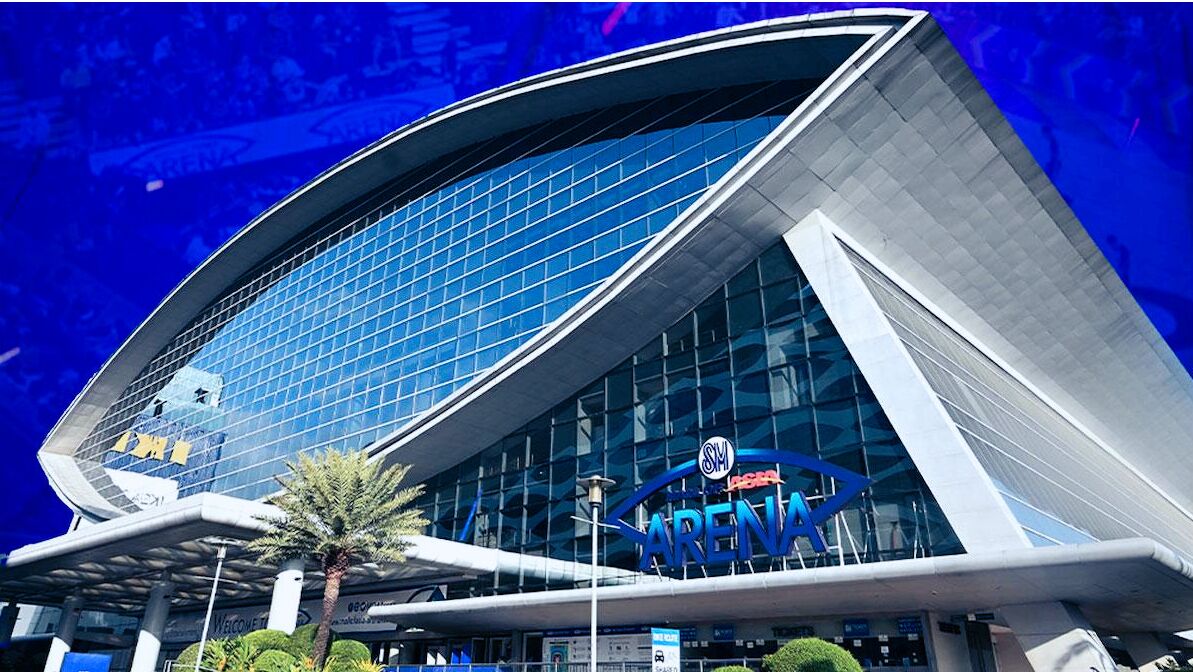 Un estadio moderno con fachada de vidrio curva y la palabra "ARENA" destacada.