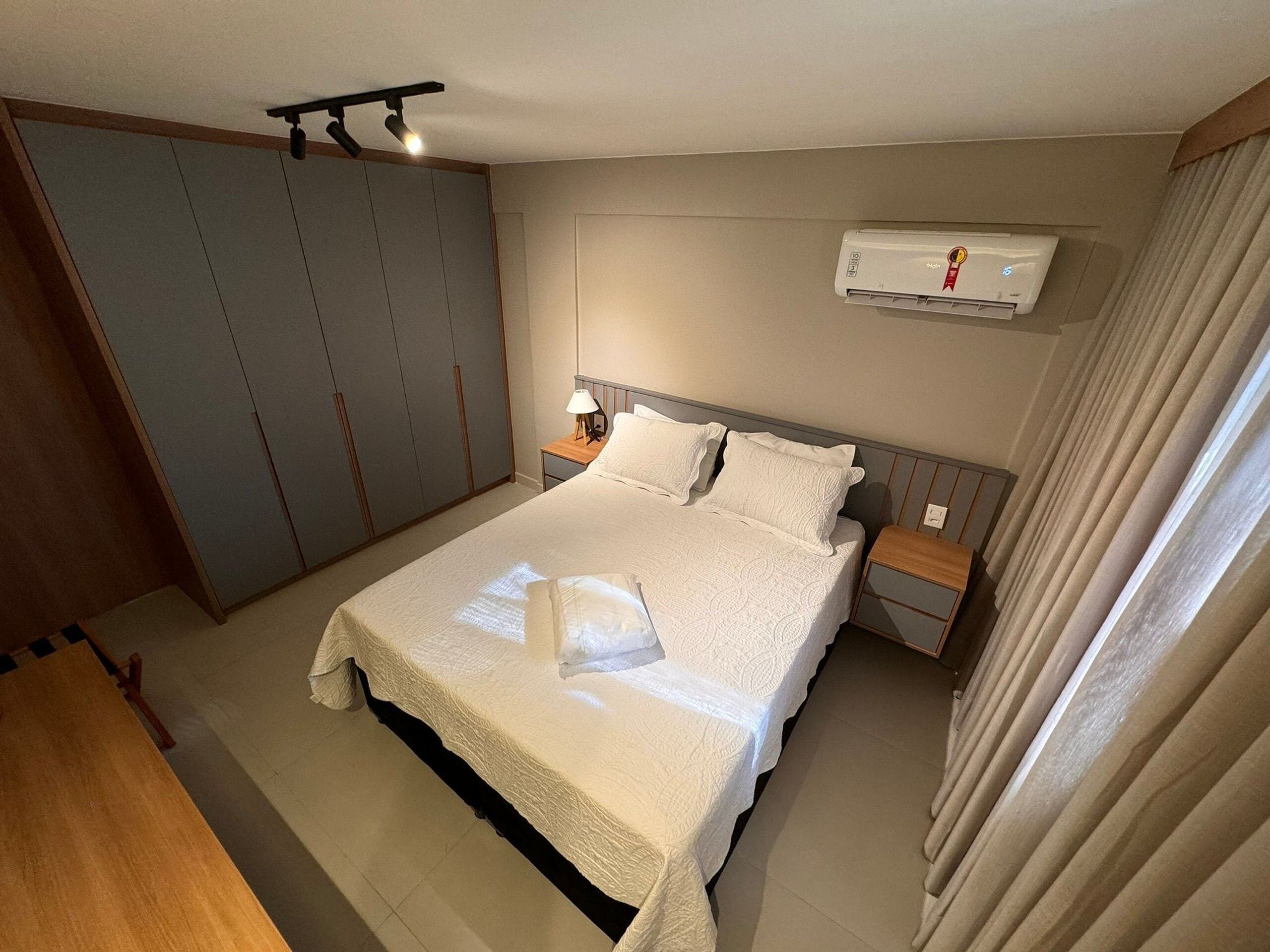 Un dormitorio ordenado con una cama grande, mesitas de noche, un equipo de aire acondicionado y un armario.