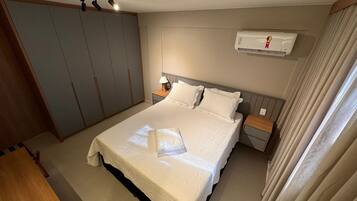 Un dormitorio ordenado con una cama grande, mesitas de noche, un equipo de aire acondicionado y un armario.