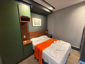 Une chambre d’hôtel avec un lit, une armoire verte, une petite table et un tableau encadré au mur.