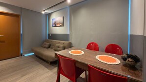 A modern dining area with a wooden table, red chairs, and a grey sofa. - Edifício Villa Oceânica  (Ipojuca)