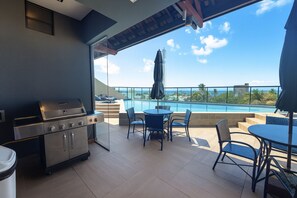 A balcony with a grill, chairs, and a view of the pool and ocean. - Edifício Villa Oceânica  (Ipojuca)