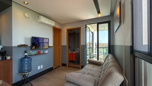 A modern living room with a sofa, a large water dispenser, a TV, and a balcony with a view. - Edifício Villa Oceânica  (Ipojuca)