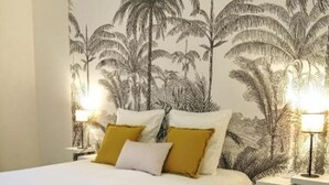 A bedroom with a bed, two bedside lamps, and a wall mural of palm trees. - Large Apartment With VIEW OF THE SEA AND CAP Canaille - free parking (Cassis)