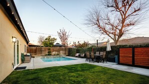A backyard with a swimming pool, a grassy lawn, and a patio area with outdoor furniture. - 5 Bedroom House in Beautiful SW Bakersfield - HWY 99 Access (Bakersfield)