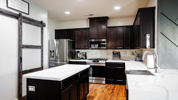 A modern kitchen with dark wood cabinets, stainless steel appliances, and a marble countertop. - 5 Bedroom House in Beautiful SW Bakersfield - HWY 99 Access (Bakersfield)