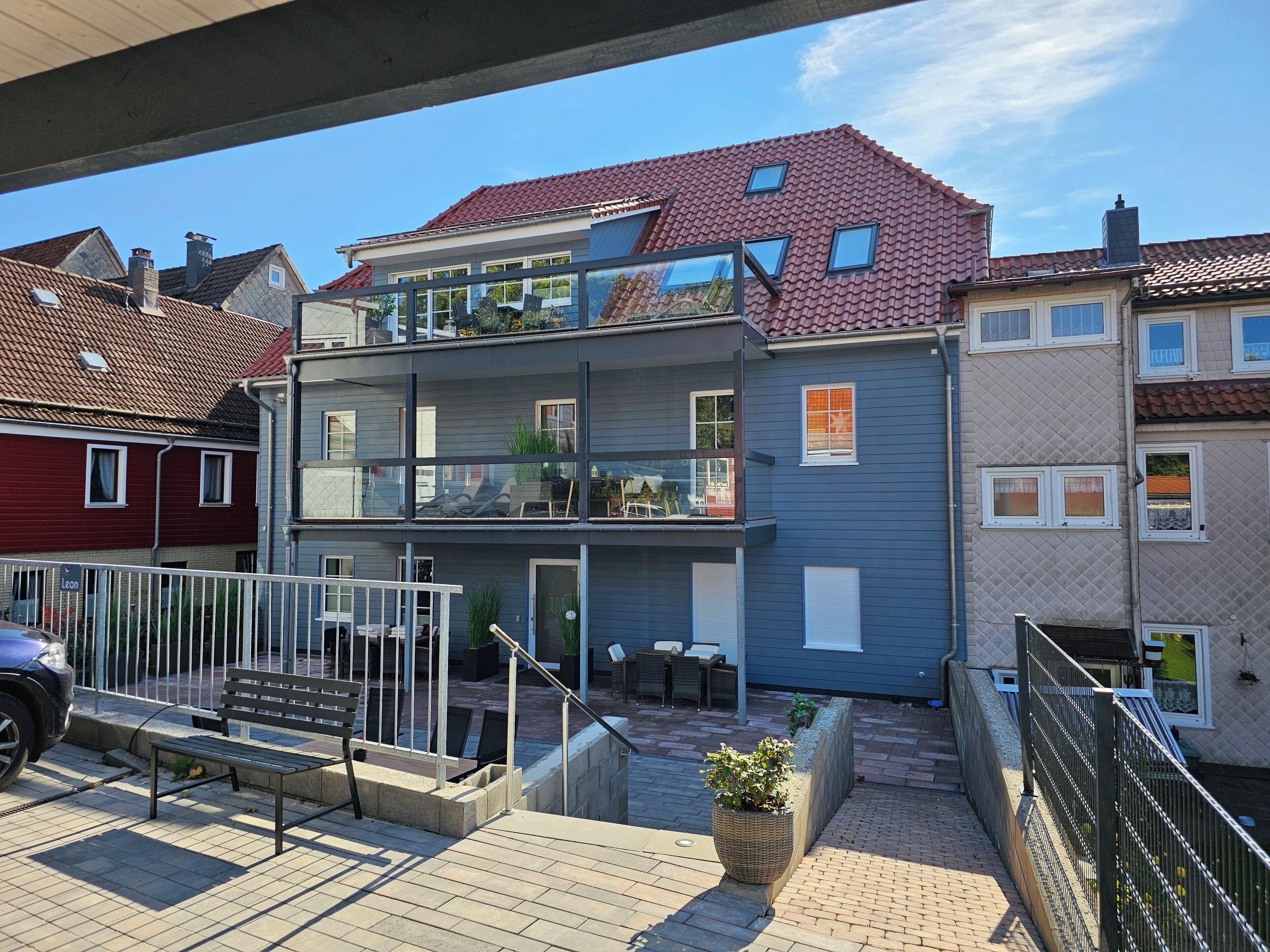 Ein modernes, zweistöckiges Wohngebäude mit Balkon, Sitzbereich im Freien und einer gepflasterten Terrasse.