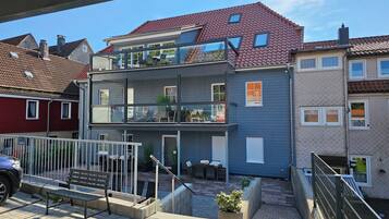 Ein modernes, zweistöckiges Wohngebäude mit Balkon, Sitzbereich im Freien und einer gepflasterten Terrasse.