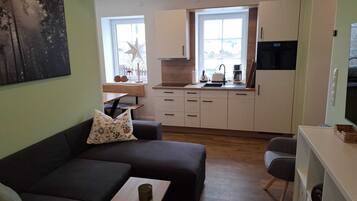 A modern living room with a sofa, a small table, and a kitchen area with cabinets and a window.