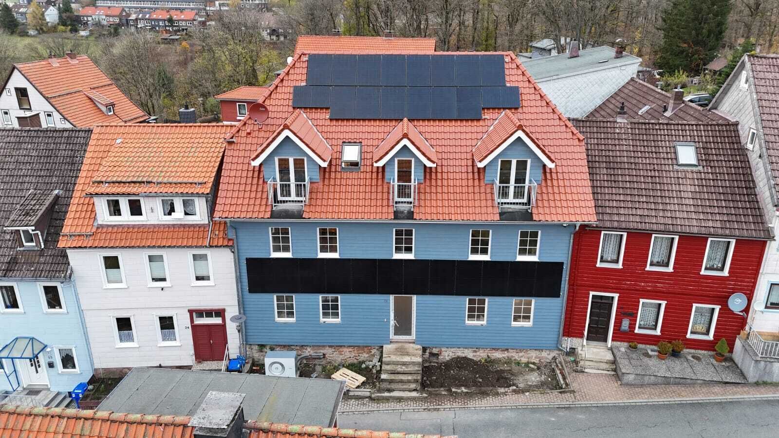 Ein mehrstöckiges Gebäude mit rotem Dach, blau-roten Fassaden und Solaranlagen.