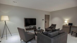 A modern living room with a flat-screen TV, a sofa, two armchairs, a coffee table, and a lamp.