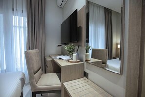 Una habitación de hotel con cama, escritorio, silla, televisión y espejo.