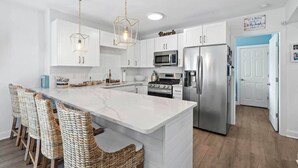 A modern kitchen with white cabinets, a central island with bar stools, stainless steel appliances, and pendant lighting.