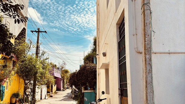 A narrow street with a motorcycle parked on the side, a sign for 'White House Beach Stay', and a building with a white facade. - Cozy Beachside Stay Near Mahabalipuram Monuments. (Mahabalipuram)