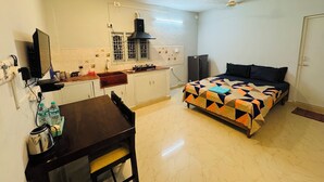 A compact room with a bed, a small kitchenette, a dining table, and a TV. - Cozy Beachside Stay Near Mahabalipuram Monuments. (Mahabalipuram)