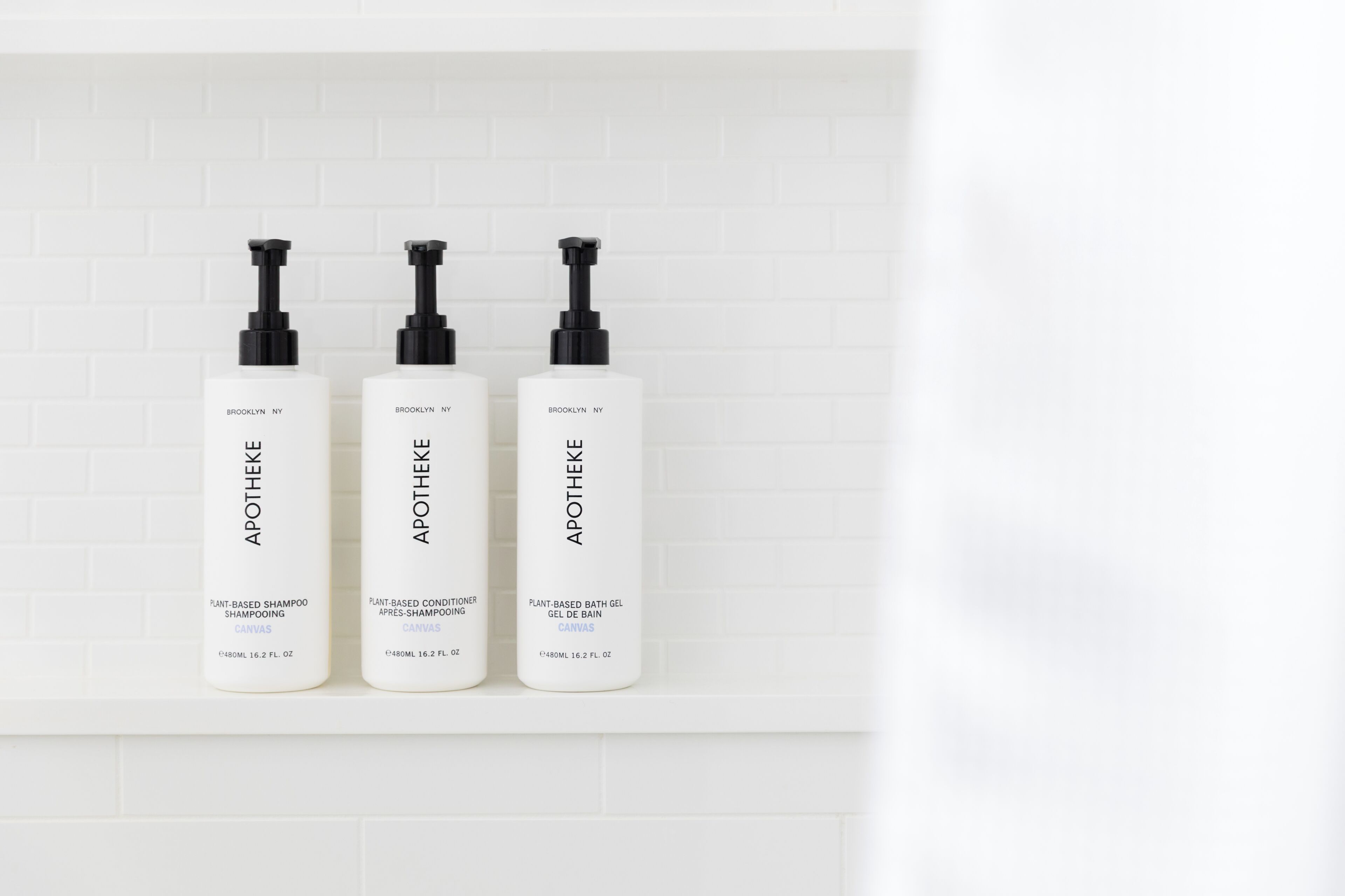 Three bottles of Apothek NY products on a white tiled wall.