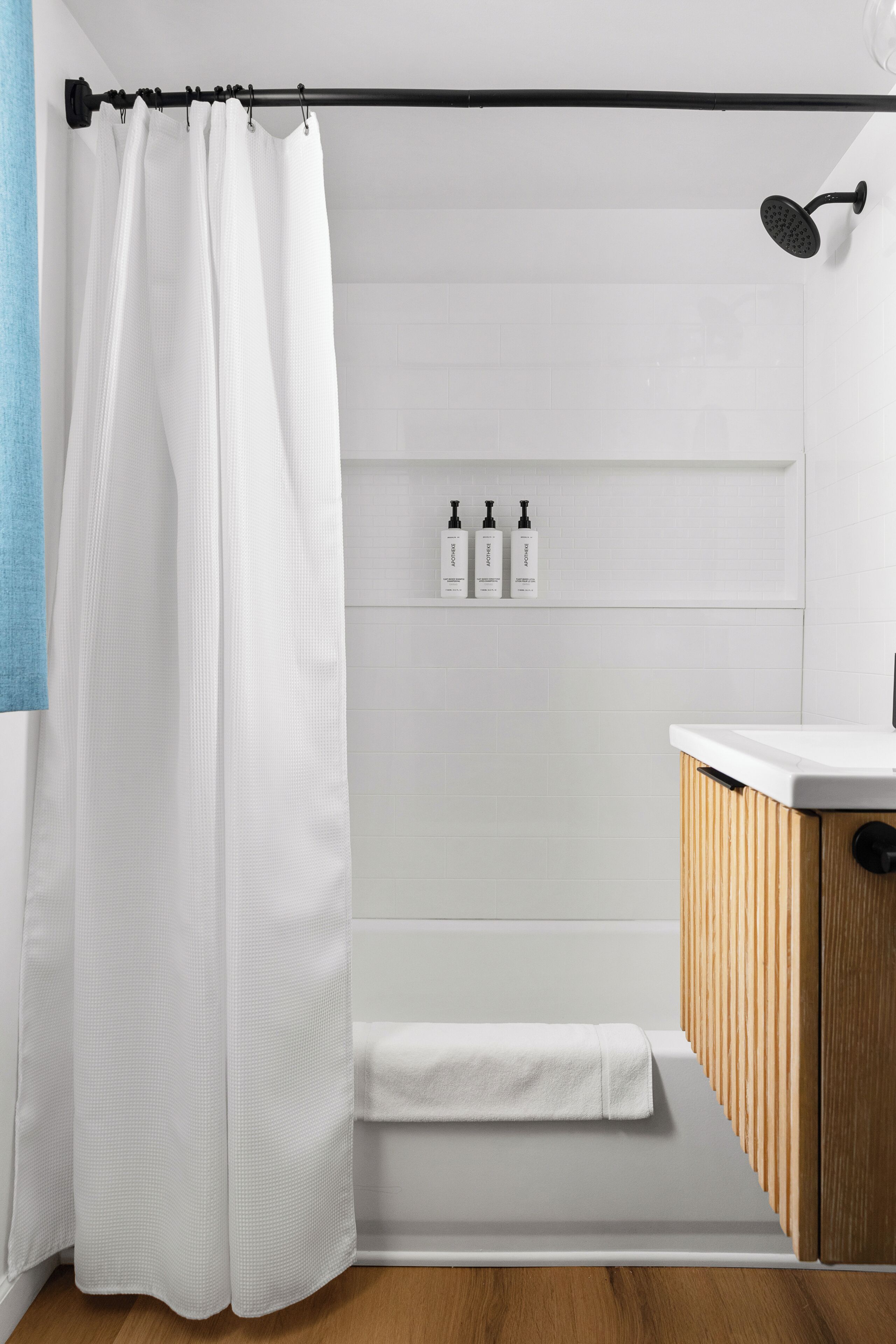 Un baño con cortina de ducha, un armario de madera, un lavabo blanco y un estante con artículos de aseo.