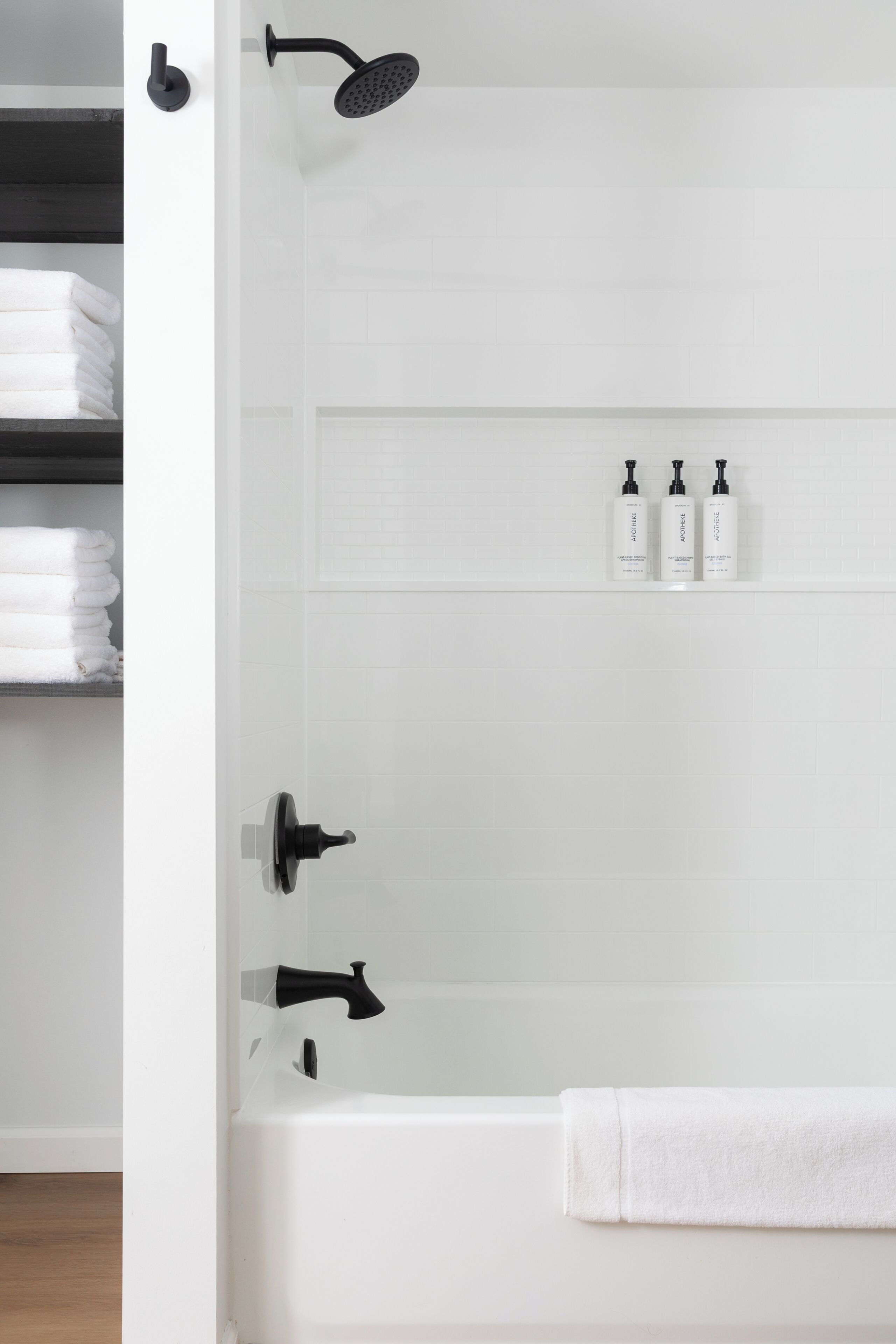 A modern bathroom with a bathtub, a showerhead, and three bottles of toiletries on a shelf.