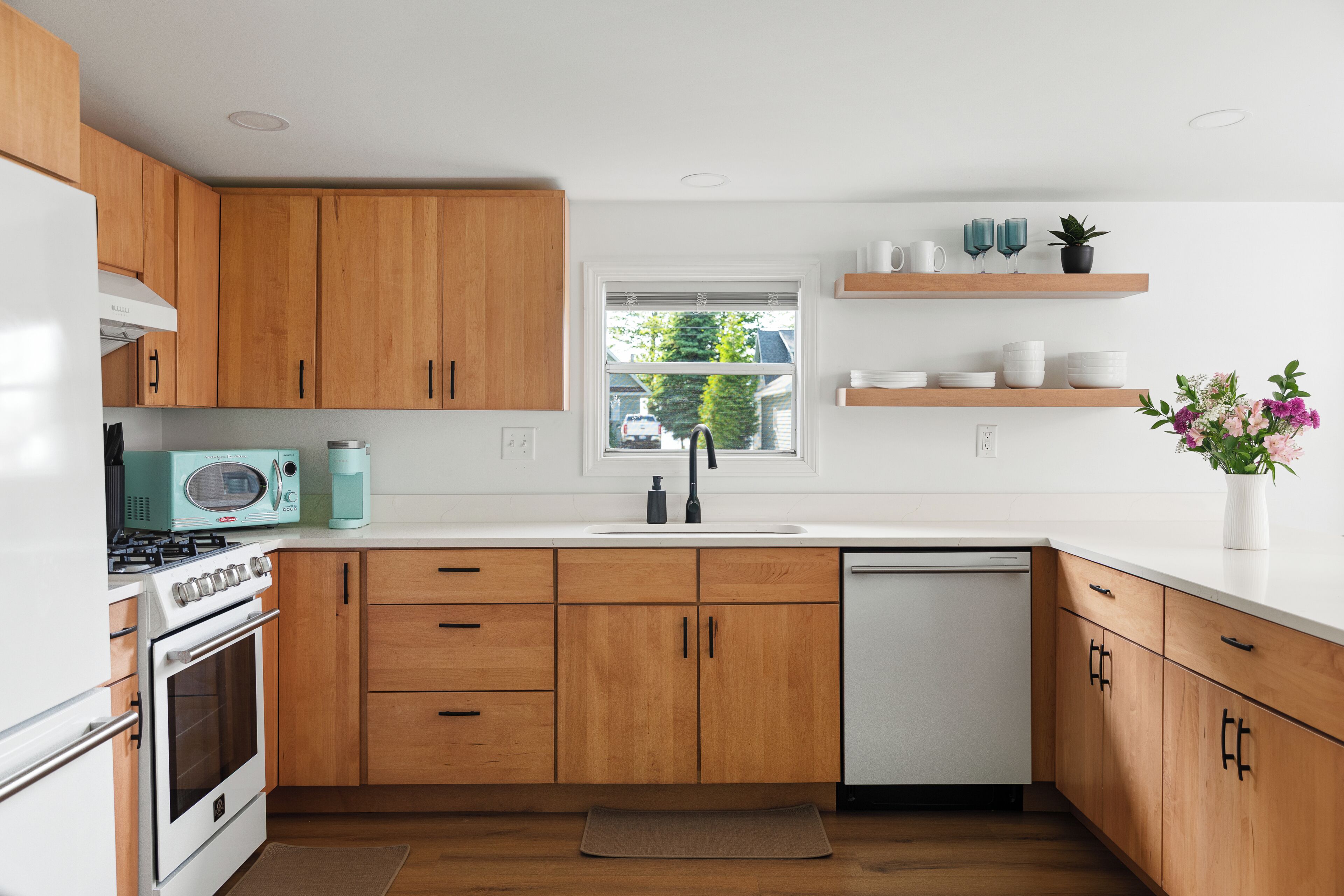 Una cocina moderna con armarios de madera, encimera blanca, microondas integrado, estufa y lavavajillas.
