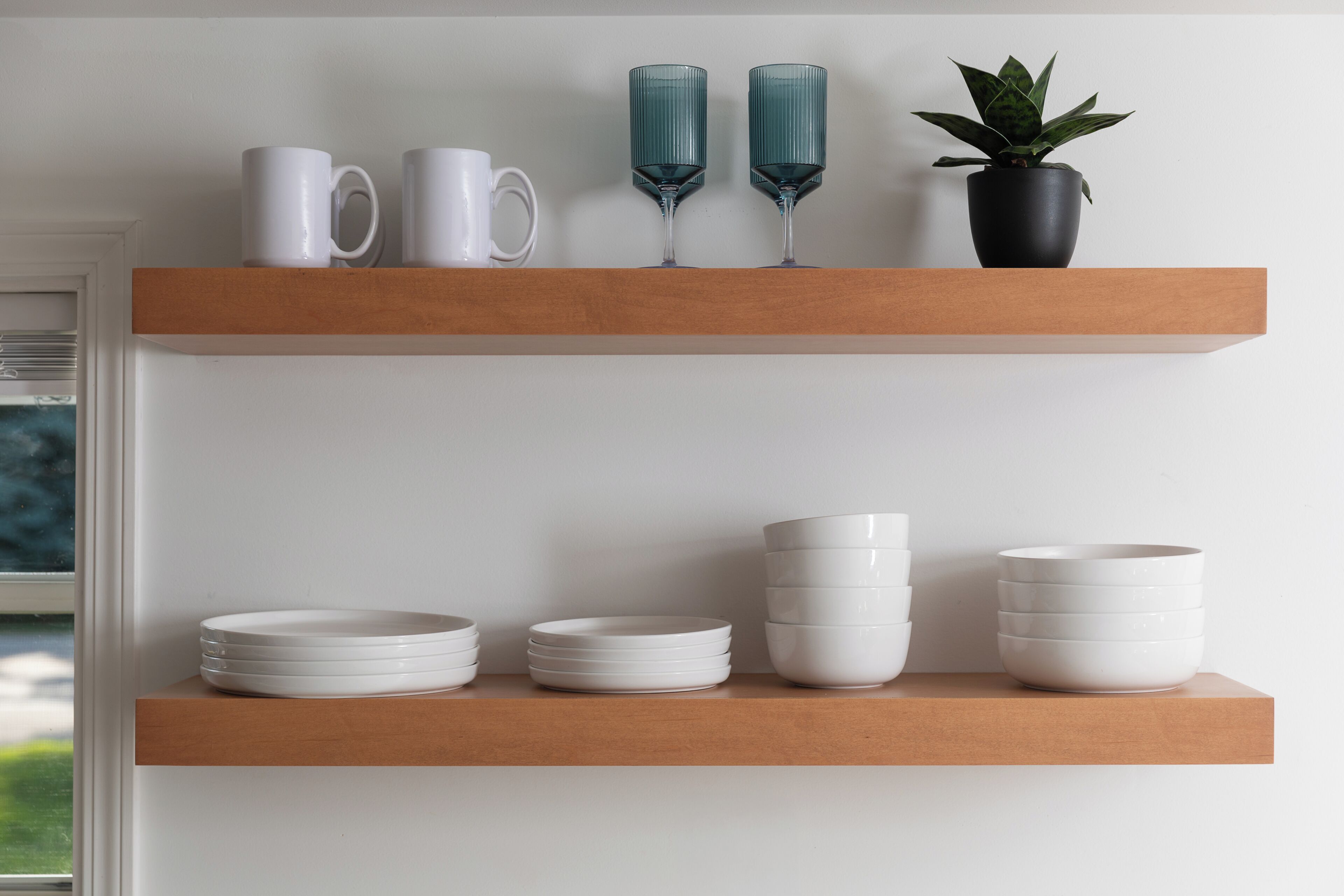 Deux étagères en bois, sur lesquelles sont disposés des verres blancs et bleus, une plante en pot et une pile d’assiettes blanches.