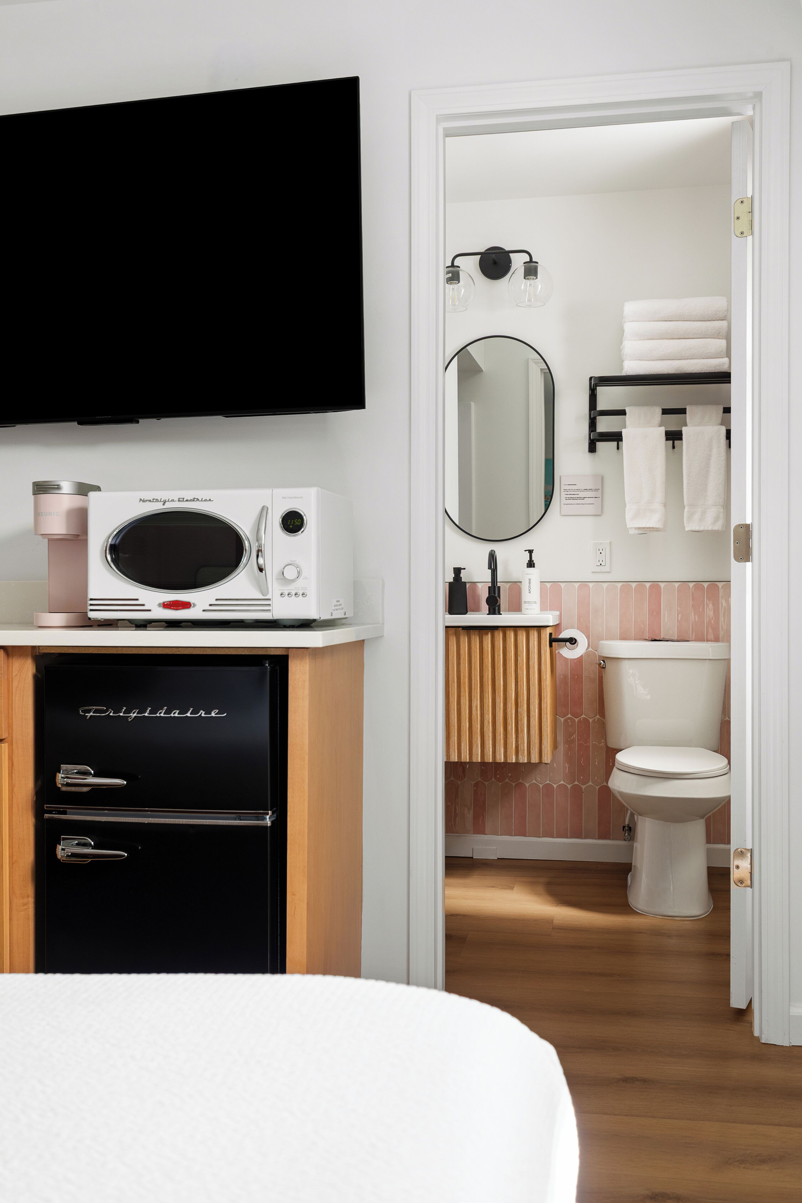 Un baño moderno con inodoro, lavabo, espejo y una cafetera sobre un mueble.