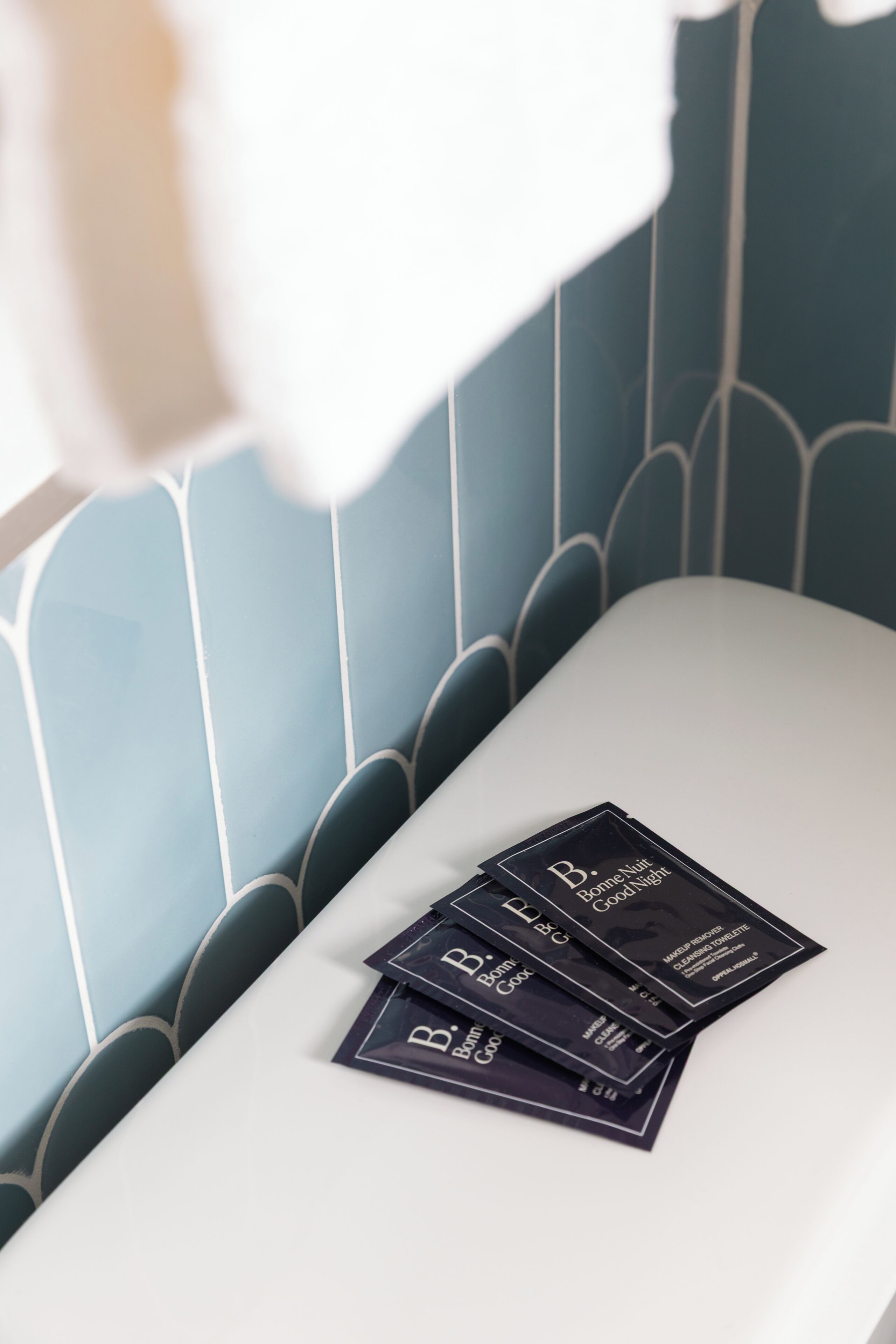 A bathroom with a white bathtub, a blue tiled wall, and three black packages on the edge of the tub.