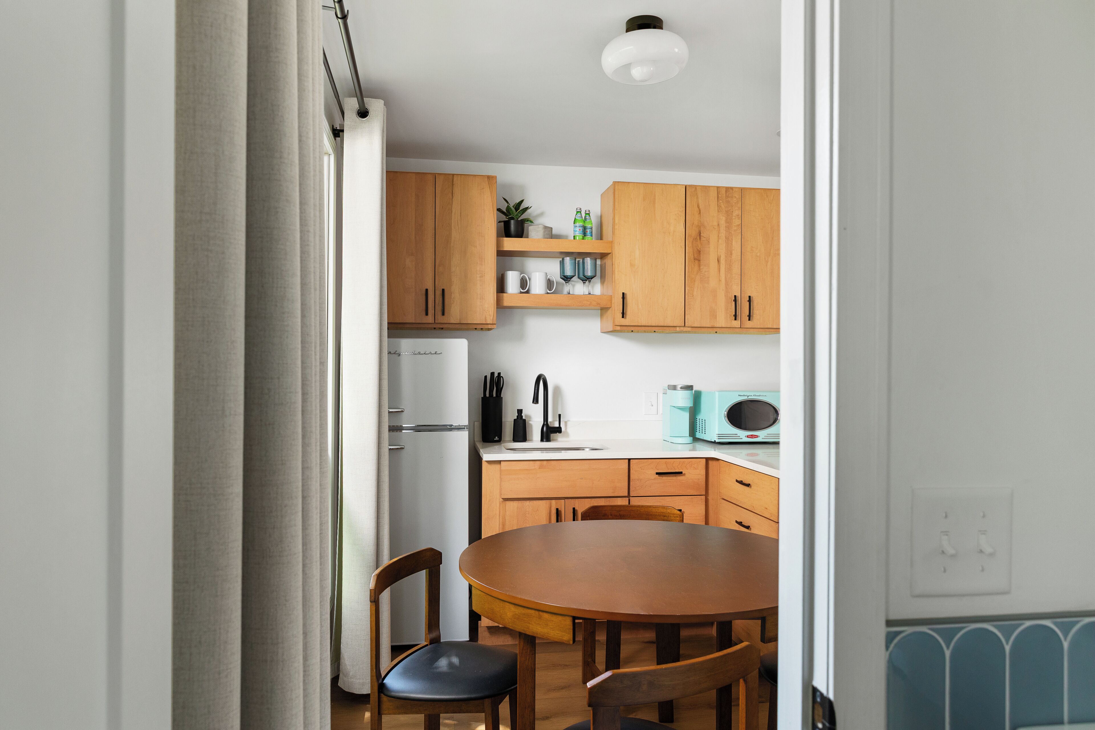 A kitchen with wooden cabinets, a white refrigerator, a dining table with chairs, and a microwave.