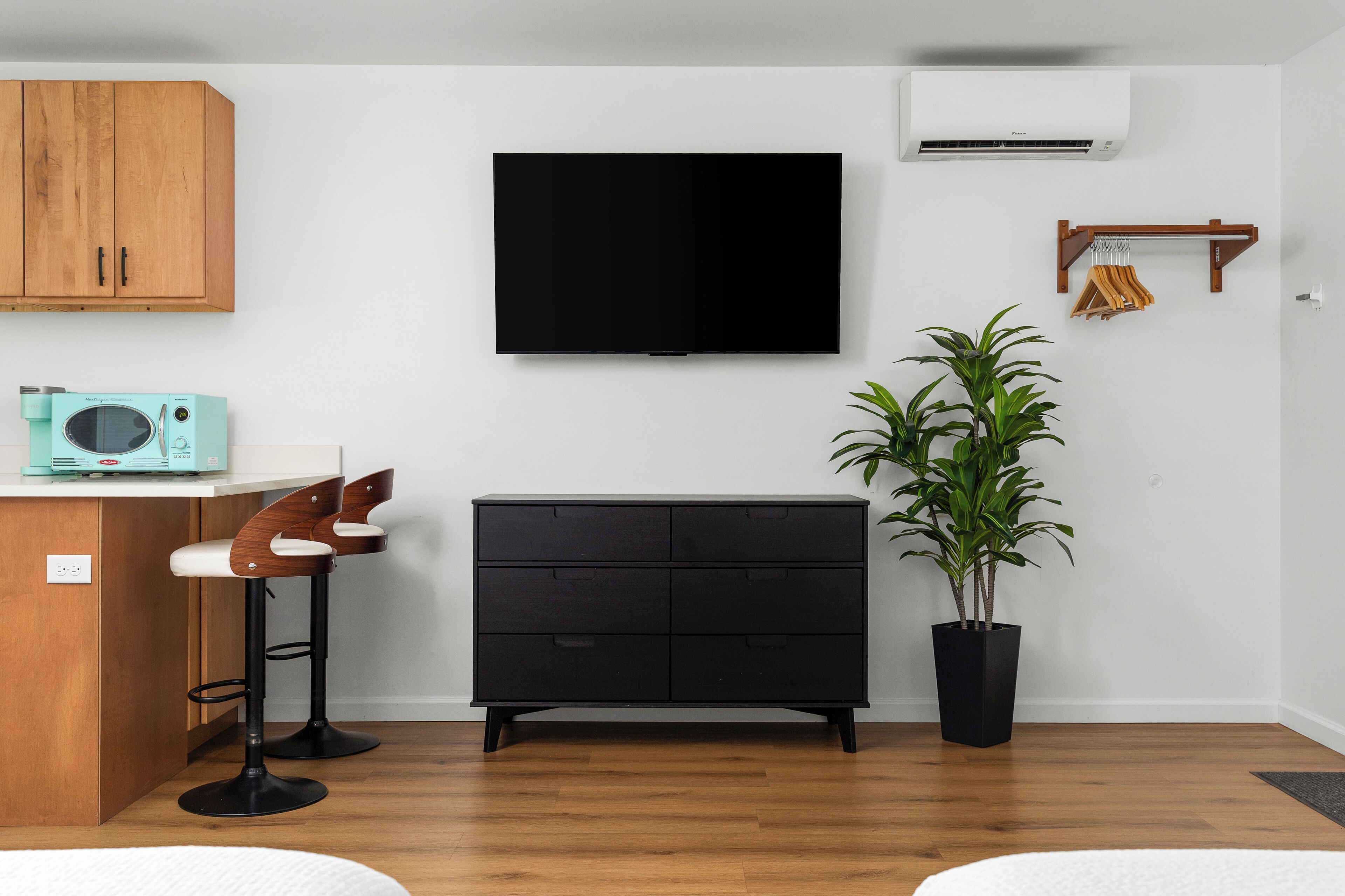Uma sala de estar moderna com televisão de tela plana, um armário preto, banquetas de madeira, uma planta em vaso e um micro-ondas.
