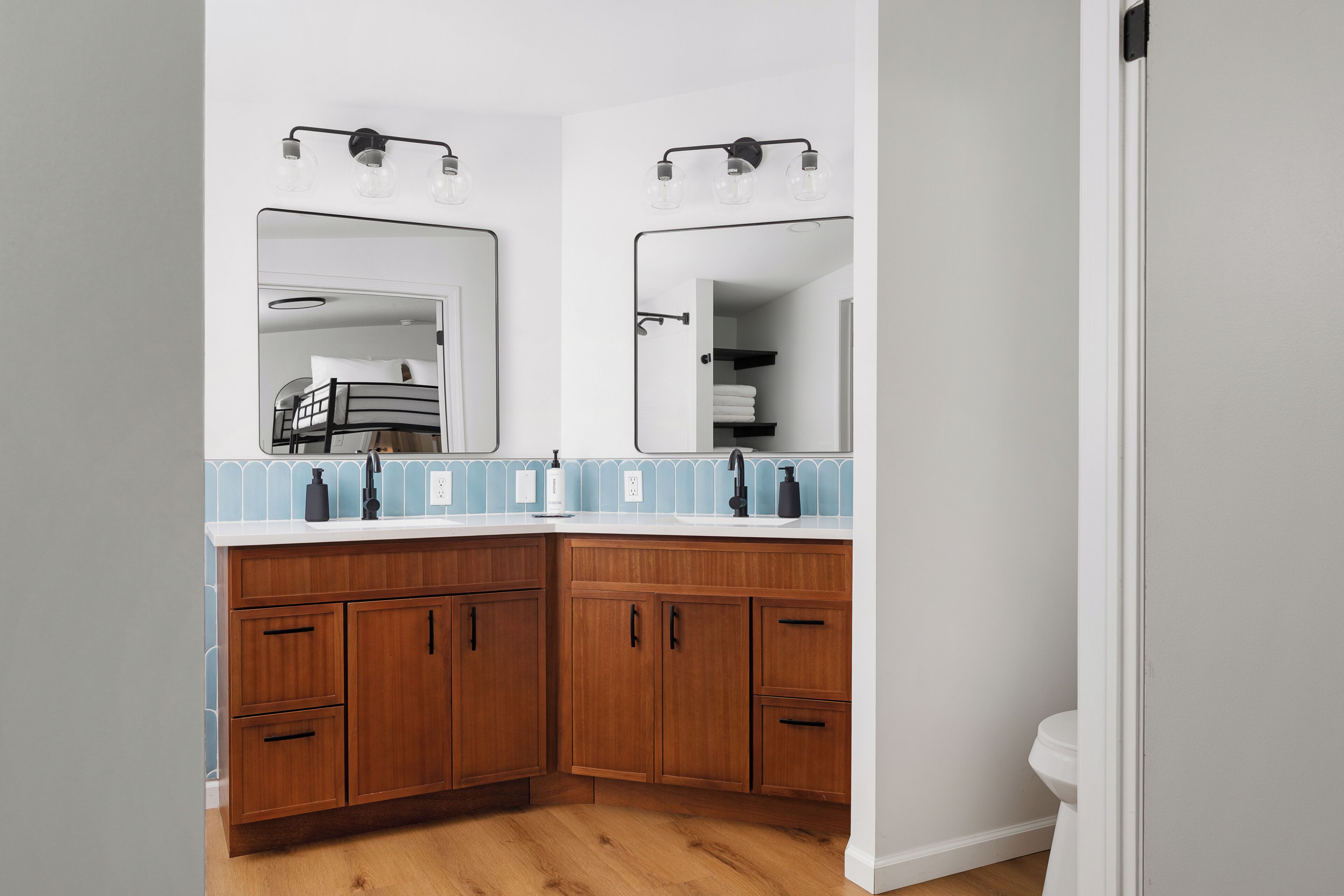 Een badkamer met een houten wastafelmeubel, twee spiegels, een wastafel en een toilet.
