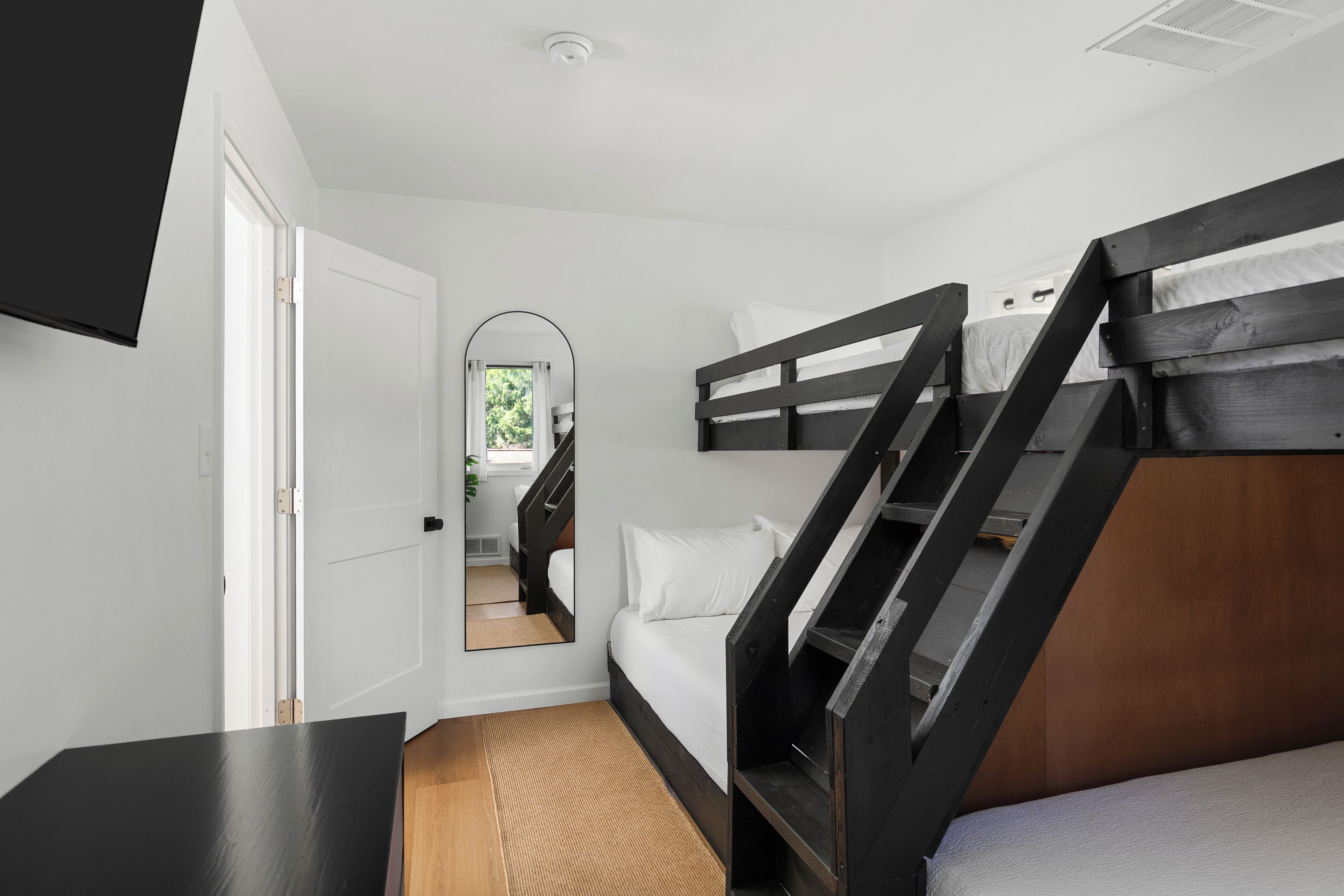 Une chambre avec un lit superposé, un bureau, un miroir et une porte donnant sur une autre pièce.