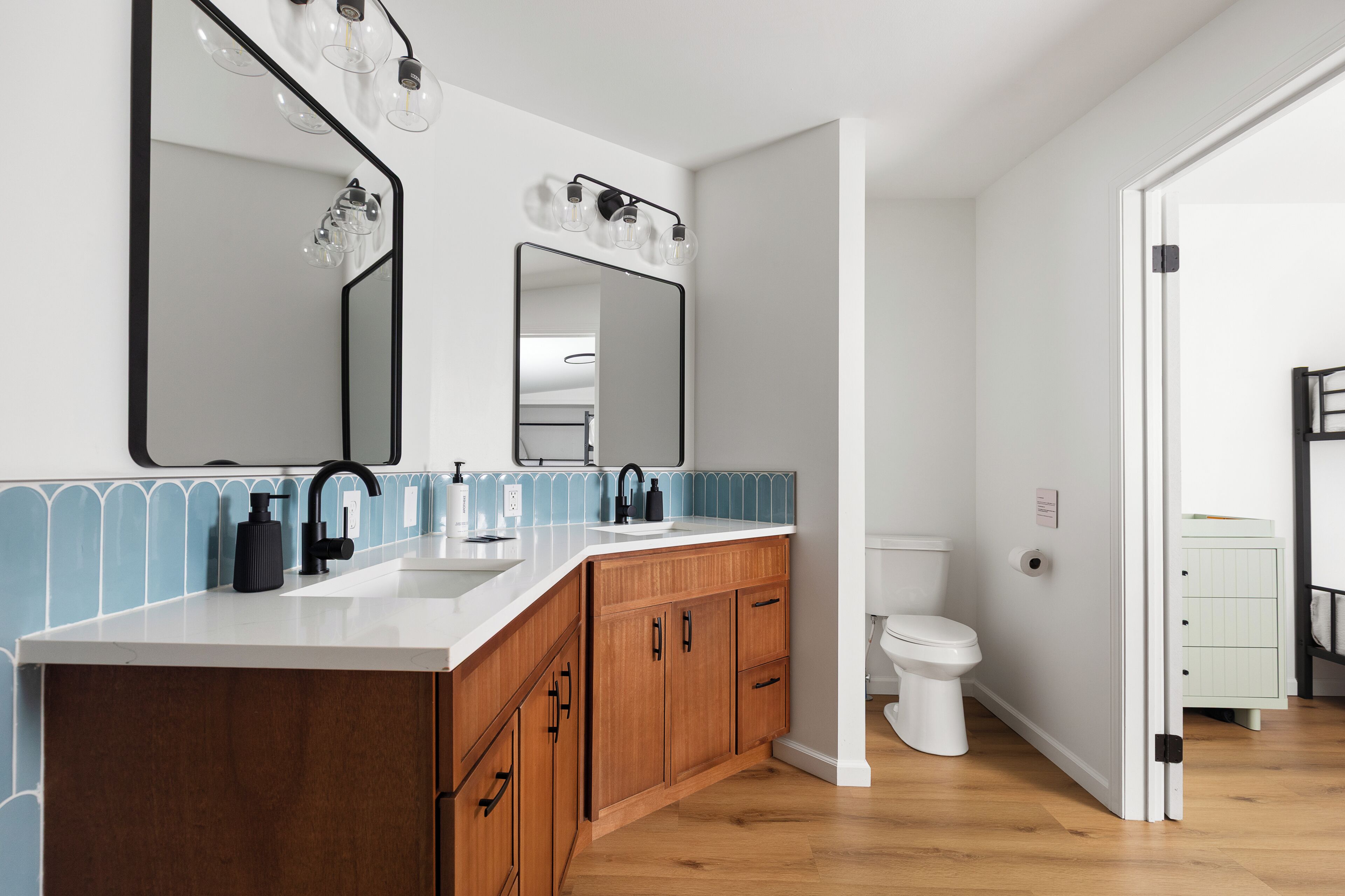 A modern bathroom with a white sink, wooden vanity, and a large mirror with lights.