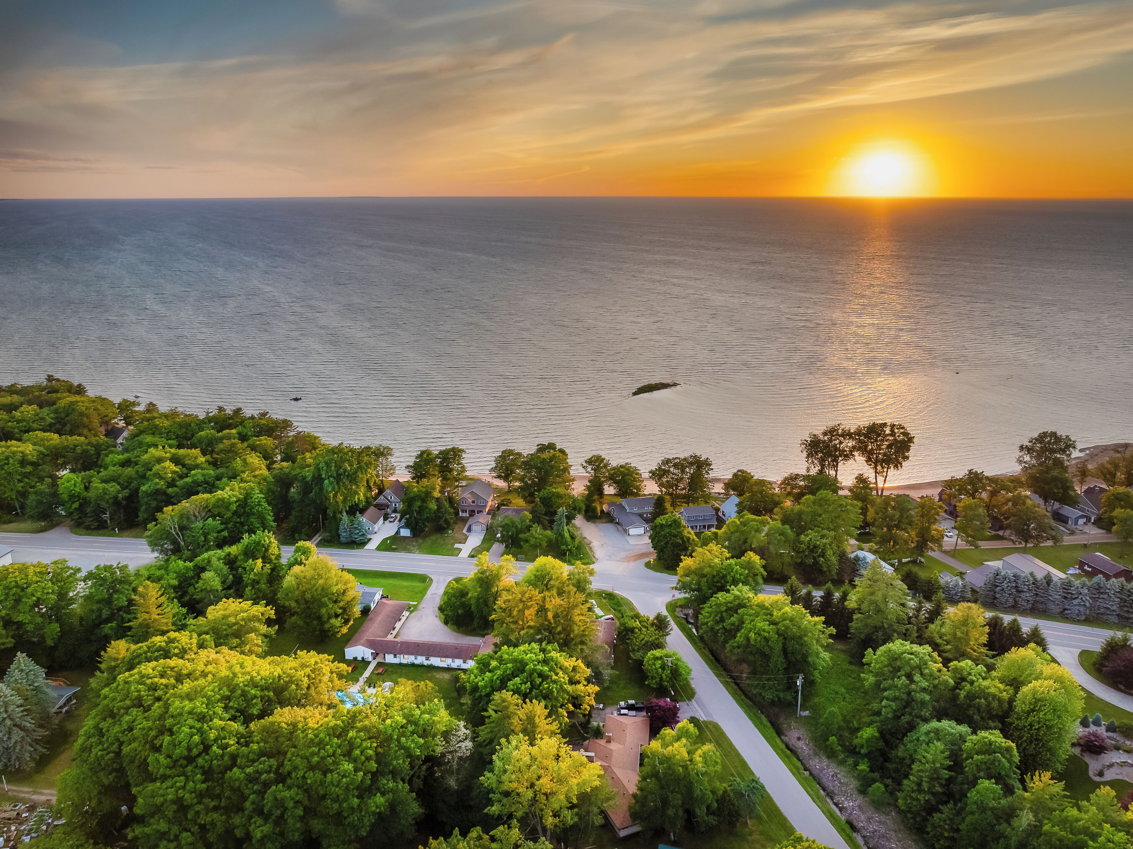 An aerial view of a residential area with houses, roads, and a body of water during sunset.