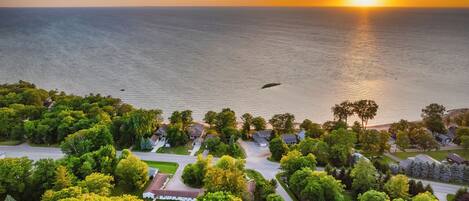 An aerial view of a residential area with houses, roads, and a body of water during sunset.