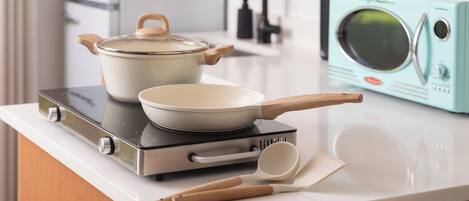 A kitchen with a stove, a pot, a pan, a microwave, and wooden utensils on a countertop.