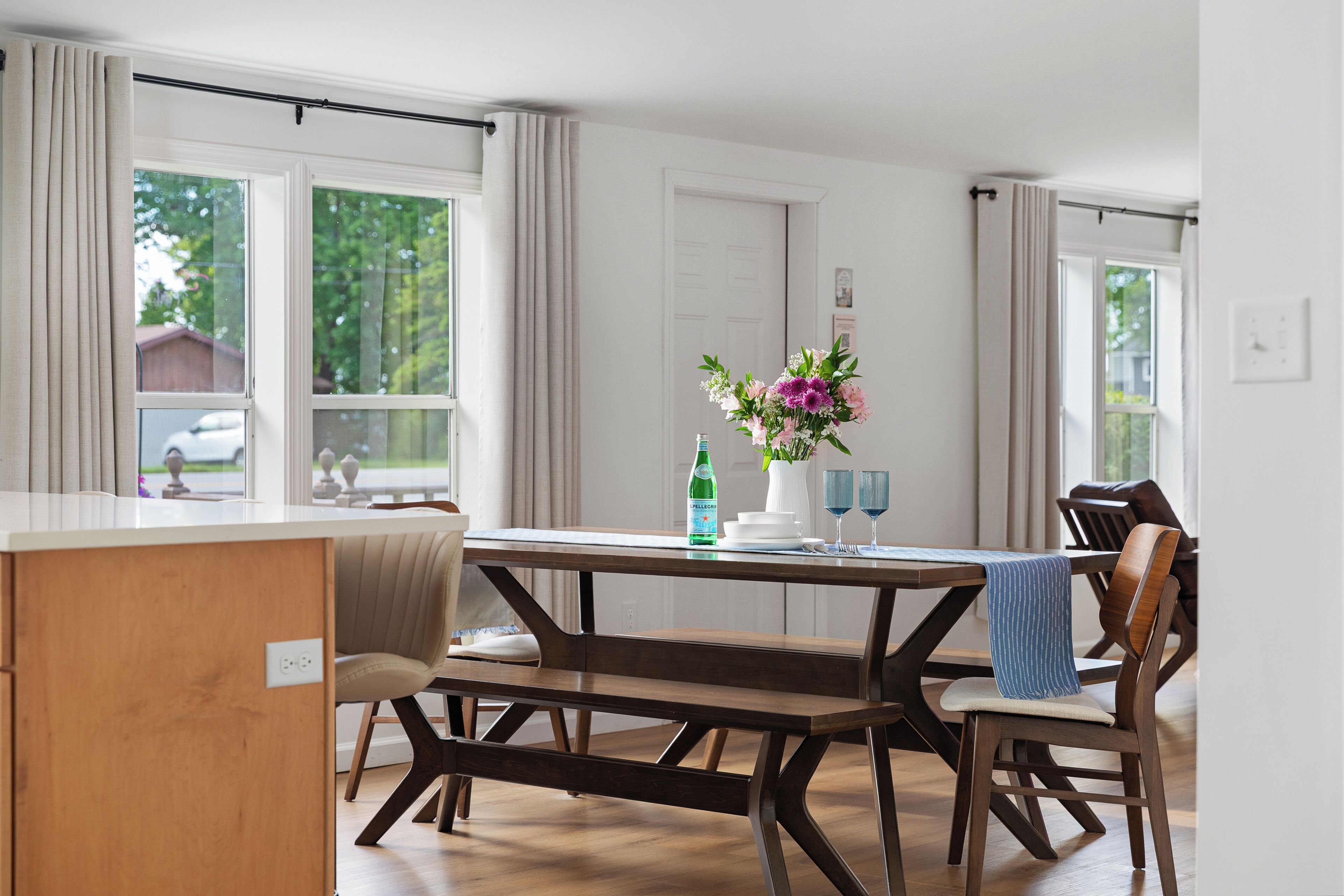A dining area with a wooden table, chairs, a bench, and a vase with flowers.