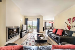 A modern living room with a fireplace, a black leather sofa, a coffee table, and a dining area with a red lamp.
