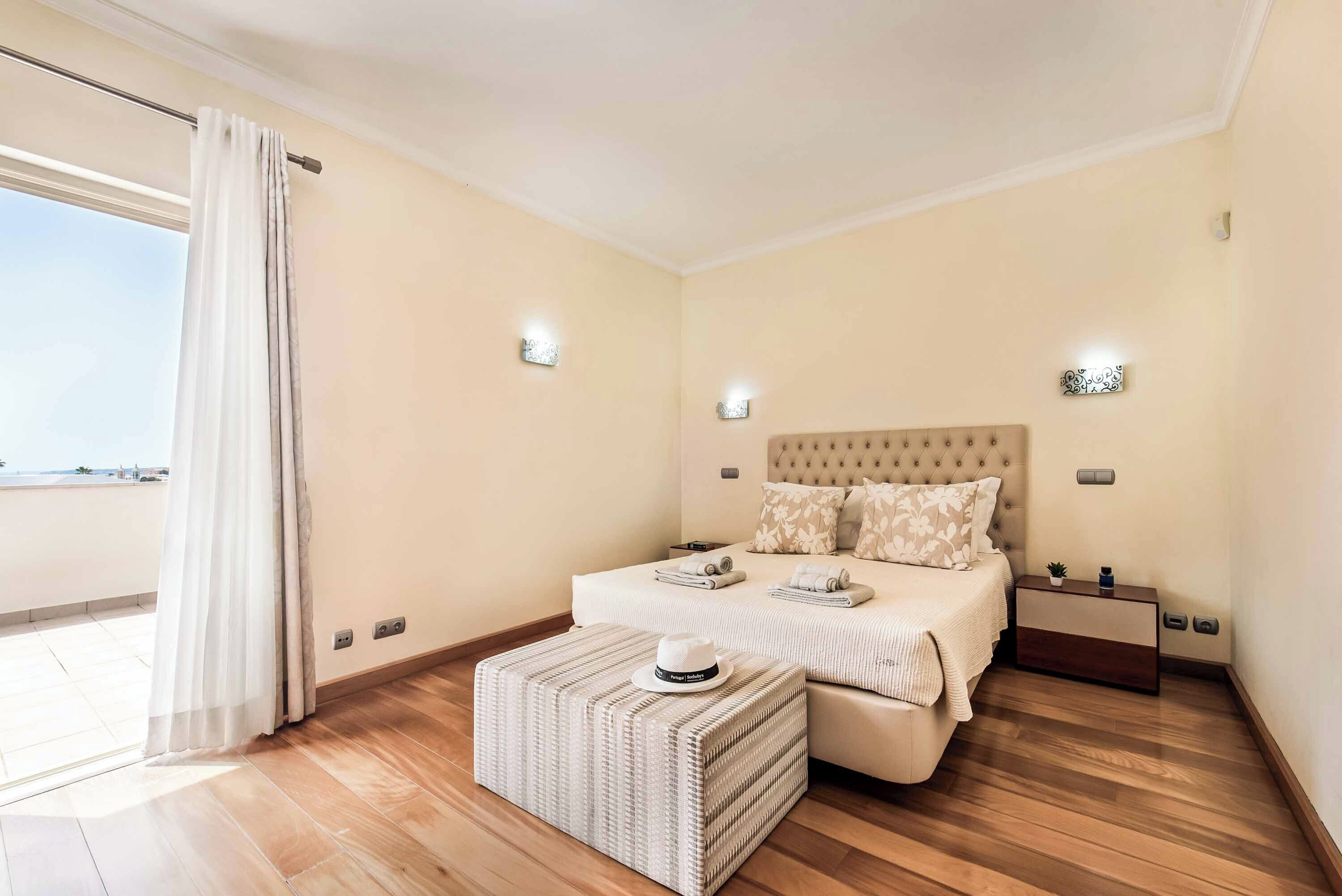 A bedroom with a bed, bedside tables, a nightstand, a window with curtains, and a view.