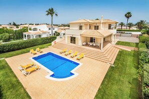 A two-story house with a swimming pool, sun loungers, and a well-maintained lawn.