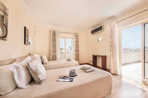 A hotel room with two beds, a flat-screen TV, a balcony with curtains, and a view of buildings.
