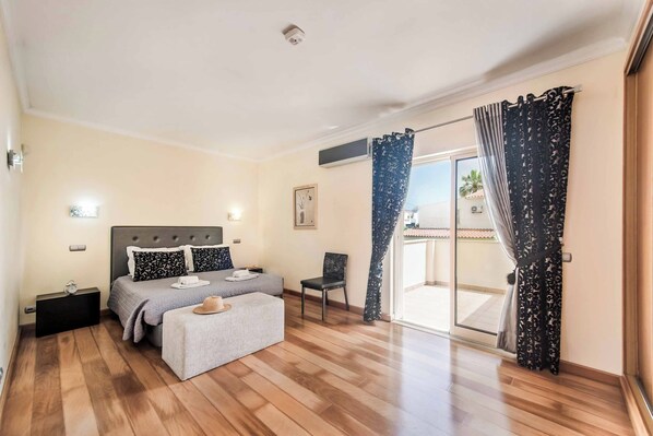 A bedroom with a bed, a chair, a nightstand, a window with curtains, and a view of the outside.