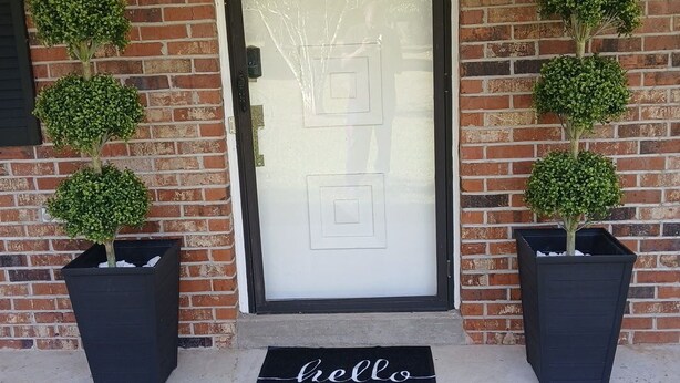 A front door with a frosted glass panel, two potted plants on either side, and a black mat with "hello" on it. - RANCH RETREAT, Beautiful 3-bedroom house in Columbus, MS (Columbus)