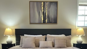 A neatly made bed with a textured beige bedspread, two bedside lamps, and a framed abstract painting above the headboard. - RANCH RETREAT, Beautiful 3-bedroom house in Columbus, MS (Columbus)