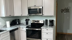 A modern kitchen with white cabinets, stainless steel appliances, and a wooden ceiling.
