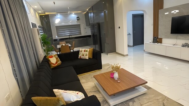 Ein modernes Wohnzimmer mit einem schwarzen Ecksofa, einem Holztisch und einem an der Wand befestigten Fernseher.