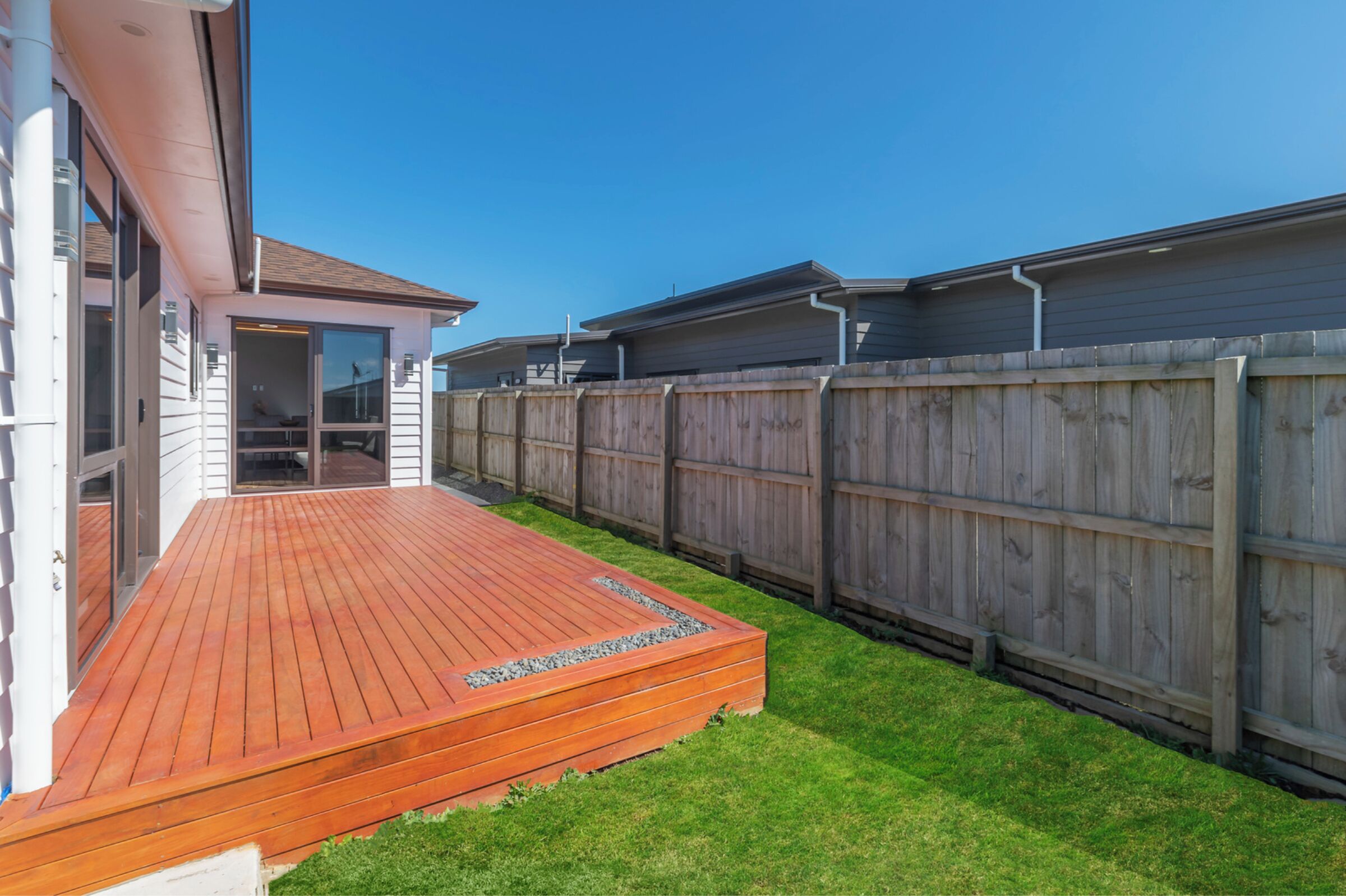 A backyard with a wooden deck, a fenced area, and a house with a garage.