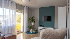 A modern living room with a sofa, a fluffy chair, a TV, and a potted plant arrangement. - Apartment MiA Cozy apartment near the Edersee and National Park (Frankenau)