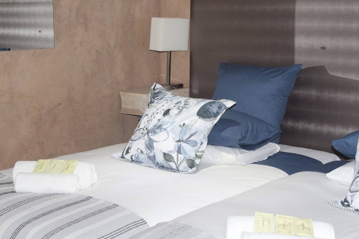 Una cama bien hecha con un cojín floral, uno azul y una toalla blanca.