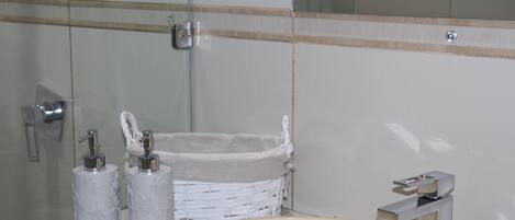 Un baño con lavamanos blanco, dos dispensadores de jabón, una cesta de mimbre blanca y un espejo.
