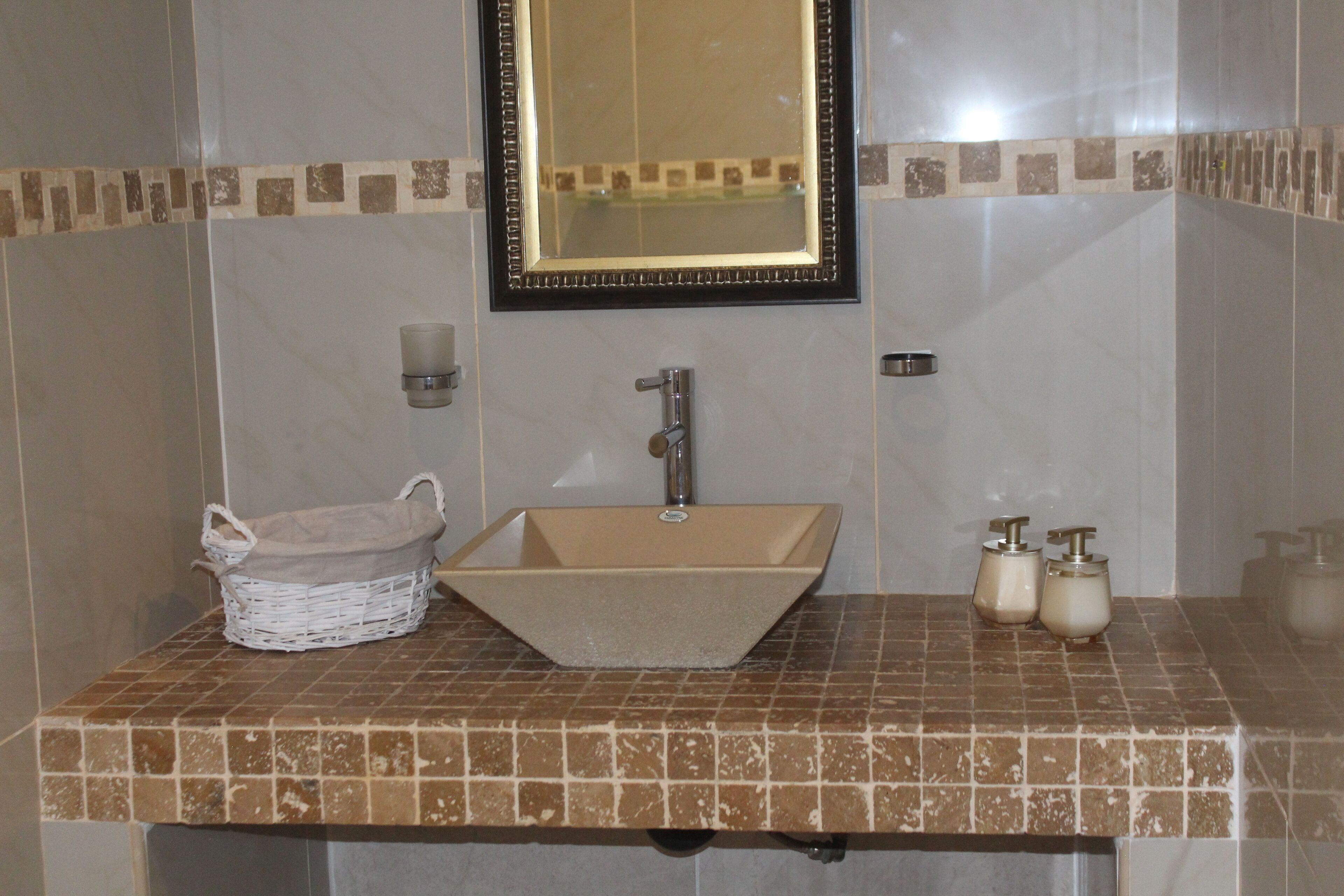 Um banheiro com pia bege, um espelho e painel de azulejos.